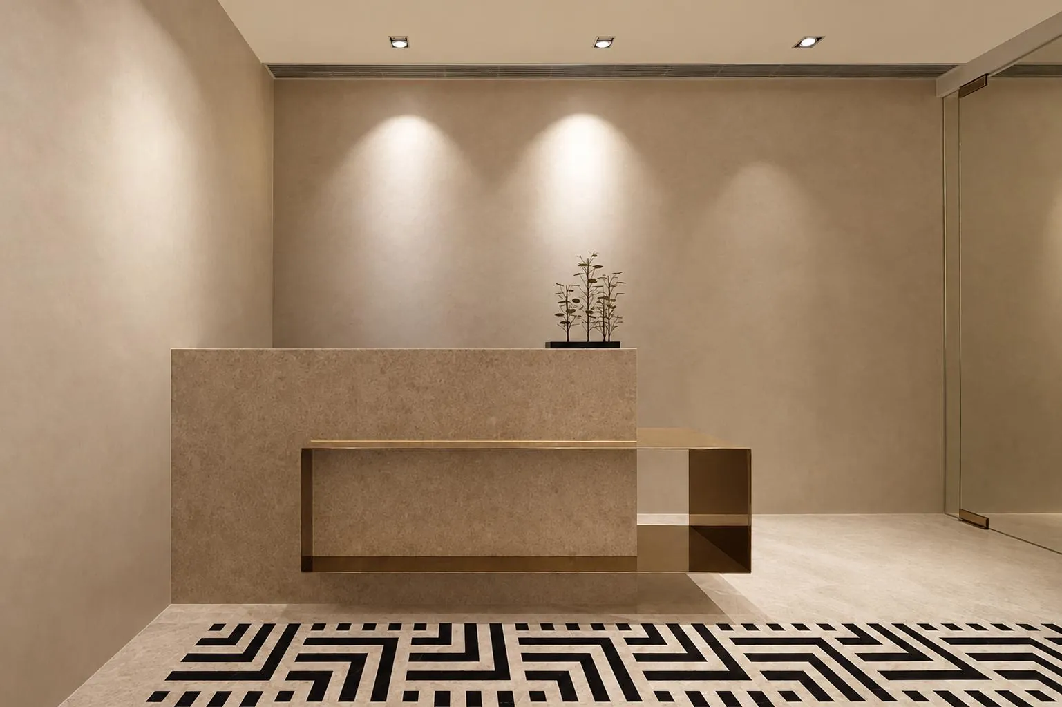 Reception desk in warm stone with a brass frame, above a black and white patterned floor
