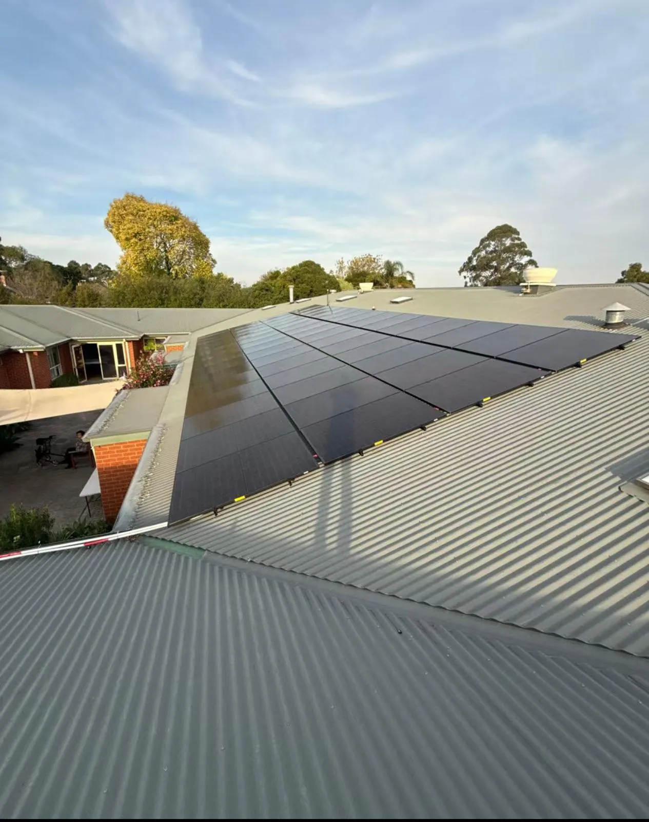 A finished array of black solar panels on a corrugated metal roof under a blue sky