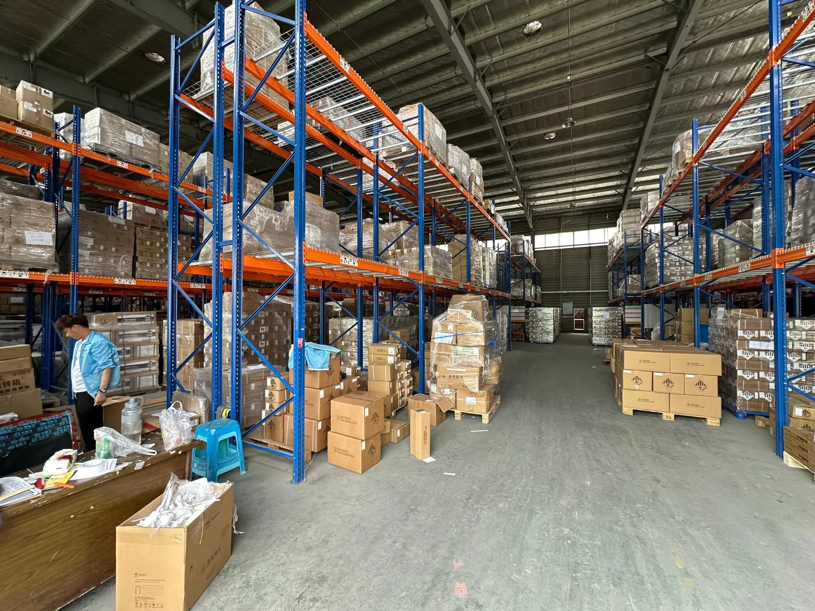 Tall blue and orange pallet racking filled with boxed stock in a large warehouse